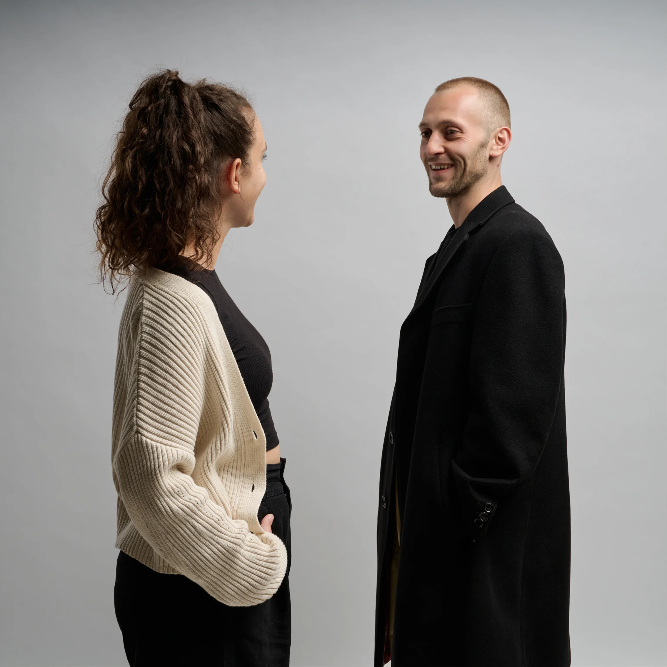 Tamara and Jan standing face to face, smiling and talking against a white background.